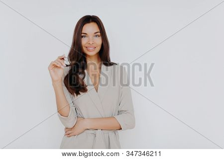 Confident Beautiful Businesswoman Touches Hair Tips, Has Gentle Smile, Wears Elegant Clothes, Stands