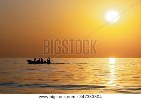 Silhouettes Of Fishermen Against A Bright Sunset With A Large Yellow Sun Under The Surface Of The Se