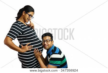 A Young Couple Showing A Pregnant Lady In Inquisitive Expression With Her Husband Placing Ear On Her