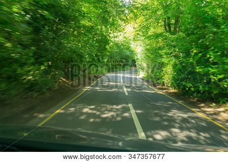 Blurred Tree Lined Road Ahead  Through Car Windscreen While Driving Along Narrow Winding Road In Sou