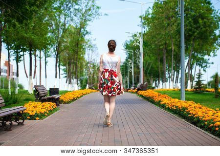 Full body portrait of a beautiful young brunette woman walking in flowers dress, summer park outdoors
