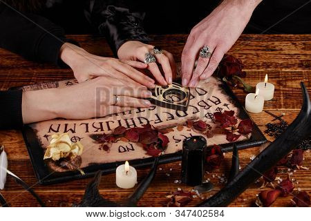 People Conducting A Seance Using A Ouija Board, Or Talking Spirit Board, With White Candles. Shot Fr