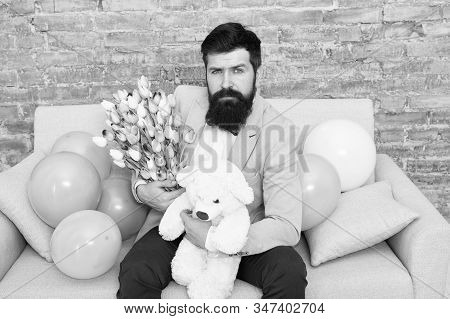 Romantic Man With Flowers And Teddy Bear Sit On Couch Waiting Girlfriend. Romantic Gift. Macho Getti