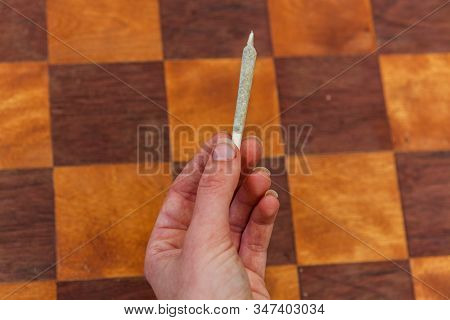Overhead Closeup Shot Of A Hand Holding A Completed Hand Rolled Marijuana Joint . In The Background 