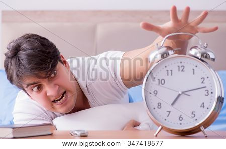 Man in bed frustrated suffering from insomnia with an alarm cloc