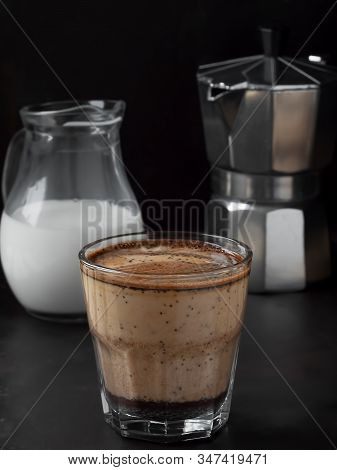 Fresh Hot Coffee In A Glass With Cream On A Black Metal Background. Near Moka Pot And Milk Jug. Clos