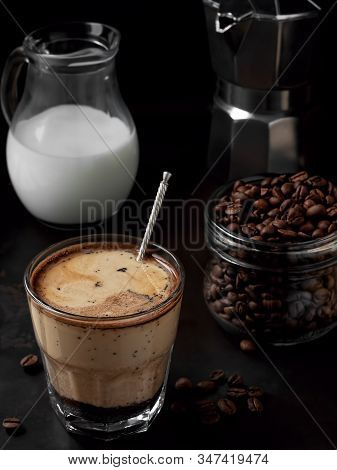 Cold Coffee In A Glass With Cream And Coffee Beans On A Black Metal Background. Near Moka Pot And Mi