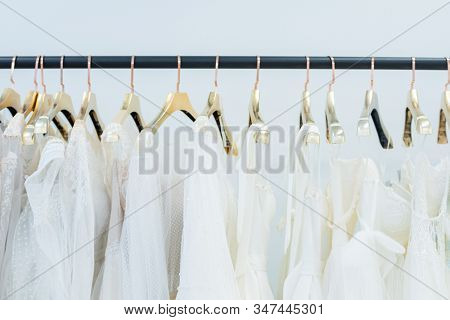 Various white dresses on hangers hanging in row on rack in wedding gown store