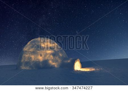 Wintry scene with snowy igloo and milky way in night sky. Fantastic winter landscape glowing by star light. Santa house from snow, ideal New Year and Christmas background
