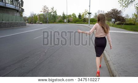 Young Beautiful Business Lady Walking On The Road And Trying To Hitch A Car