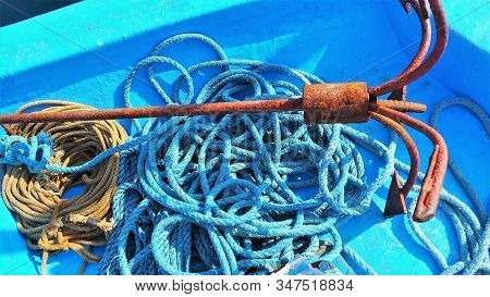 Blue Wooden Boat With Blue And Yellow Rope And Rusty Anchor.