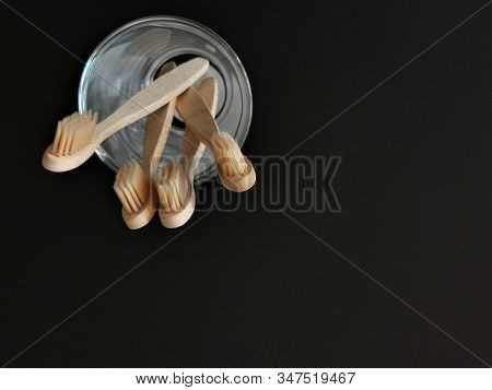 A Family Set Of Four Wooden Toothbrushes In A Glass On Black Background With Copy Space