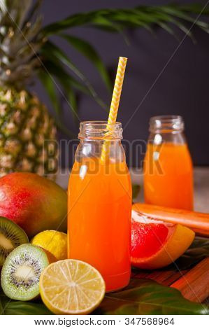 Two Bottles Of Tropical Exotic Multifruit Juice Under A Palm Leaves With Fruits On The Background.