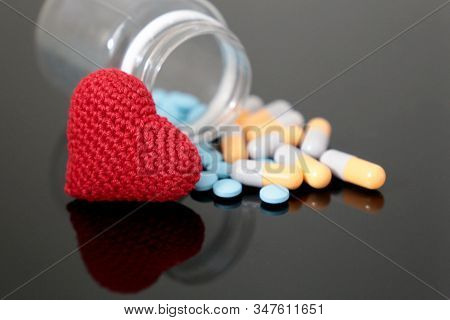 Pills And Knitted Red Heart On Dark Glass Table, Bottle With Medication In Capsules. Concept Of Hype
