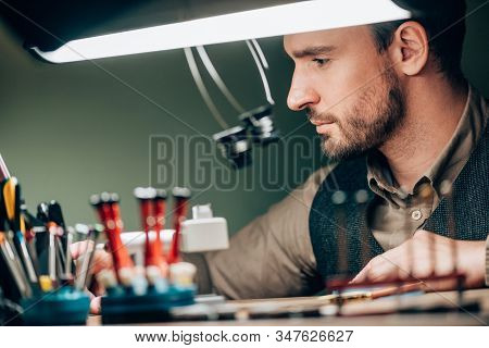 Selective Focus Of Handsome Watchmaker Working With Equipment At Table