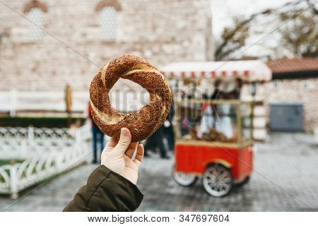 A Person Is Holding A Traditional Turkish Bagel Simit On The Background Of A Street Stall Selling Si