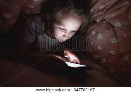 A Young Little Girl Is Hiding Under A Blanket To Use A Digital Tablet Smartphone Device Late After S