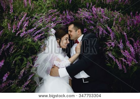 Couple At Sunset In A Wedding Dress Lie On The Grass With Lipin Flowers,festive Spring Wedding Photo