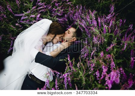 Couple At Sunset In A Wedding Dress Lie On The Grass With Lipin Flowers,festive Spring Wedding Photo