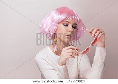 Portrait of teenage model with pink hair posing against pastel background. Studio photo of funky teenager wearing color wig and trendy glasses.