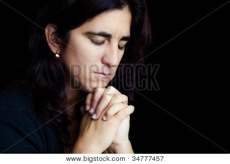 Retrato dramático de uma mulher hispânica triste rezando isolado em preto com espaço para texto
