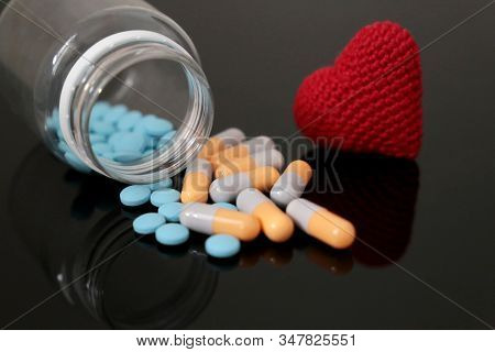 Pills And Knitted Red Heart On Dark Glass Table, Bottle With Medication In Capsules. Concept Of Hype