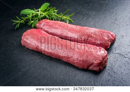Raw dry aged venison tenderloin fillet steak natural with herbs offered as closeup on a modern design board 