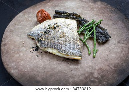 Japanese gourmet fried gilthead fish filet with glasswort, umeboshi and algae as closeup on a modern design plate 