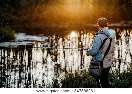 A Man Fisherman Fishing In The River With A Fishing Rod