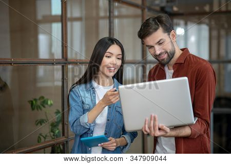 Beraded Handsome Man In A Brown Shirt And His Female Colleague Looking At The Laptop