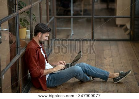 Beraded Handsome Man In A Brown Shirt Sitting On The Floor And Looking Concentrated