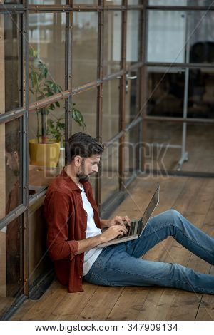 Beraded Handsome Man In A Brown Shirt Sitting On The Floor And Working