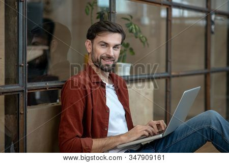 Beraded Handsome Man In A Brown Shirt Sitting On The Floor