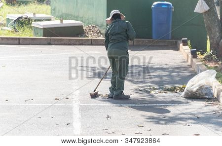 A Close Up View Of A Municipal Worker Sweeping The Leaaves On The Edge Of A Parking Area