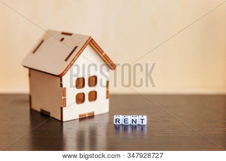 Miniature Toy Model House With Inscription Rent Letters Word On Wooden Backdrop. Eco Village Abstrac