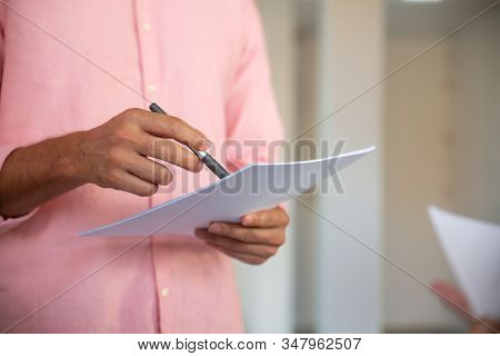 Closeup Shot Of Male Hands Holding Paper Sheet And Pen. Cropped Shot Of Young Man Pointing With Pen 