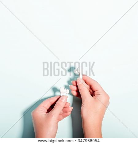 White Wireless Earphones In Female Hand On Pastel Background, Copy Space. Modern Technology Flat Lay