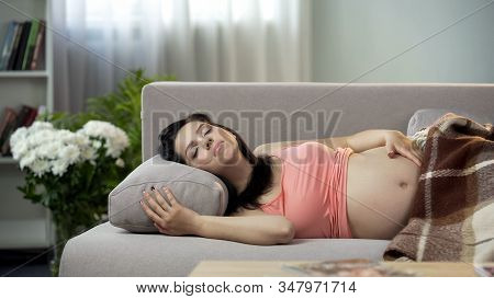 Relaxed Pregnant Lady Sweetly Sleeping On Sofa, Hugging Her Tummy With Baby