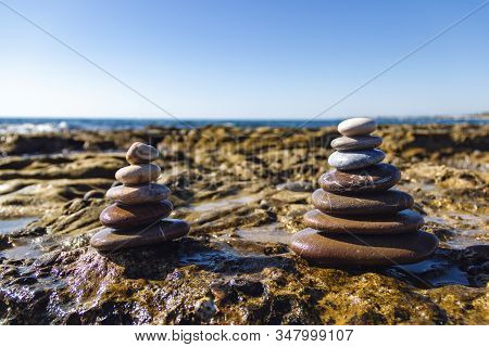 Pyramids Of Stones For Meditation Lying On Sea Coast. Stack Of Stones Against Blurred Seascape, Spac