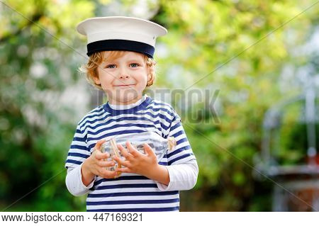 Happy Little Kid Boy In Sailor Capitain Hat And Uniform Playing With Sailor Boat Ship. Smiling Presc