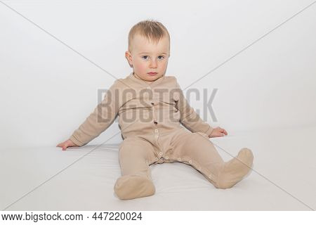 A Little Boy In Pajamas Sits On A White Sheet. Time To Fall Asleep
