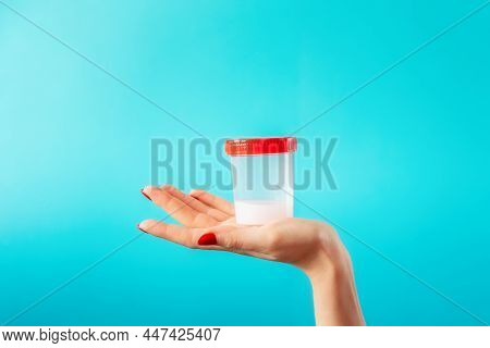 A Female's Palm Holds A Plastic Jar With A Sample Of Sperm. Close-up Of A Hand On A Blue Background 