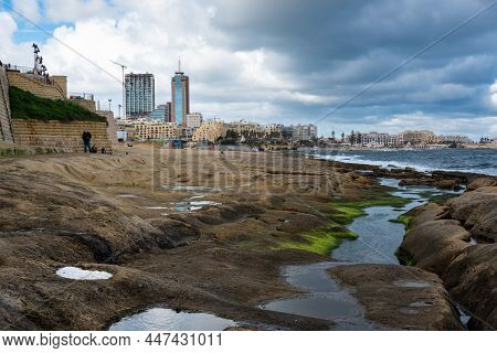 Saint Julian, Malta - 01 07 2022: Low Angle View Over The Water, Rocks And Sand At The Beach With Th
