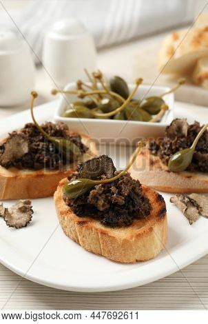 Delicious Bruschettas With Truffle Sauce And Caperberries On White Wooden Table, Closeup