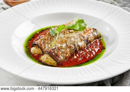 Eggplant rolls stuffed with tomato and cheese. Baked eggplant and cheese rollatini. Eggplant appetizer in white plate on stone background. Plant-based menu