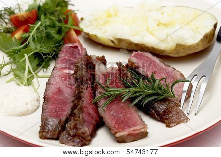 Closeup on slices of grilled gourmet wagyu rib-eye steak served with horseradish sauce, a baked potato and a fresh green salad