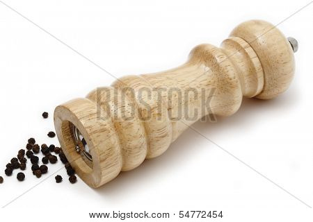 A traditional wooden peppermill lying on its side, with a scattering of peppercorns nearby