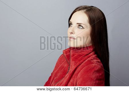 Portrait of a young business woman on gray studio background, wearing red suede leather jacket with long brunette hair