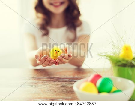 easter, holiday and child concept - close up of girl holding yellow chiken toy with green grass in pot and bowl of colored eggs