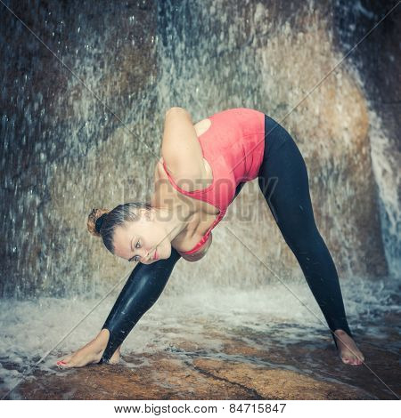 Woman practicing yoga near waterfall. Wide-Legged Forward Bend. Parsva Prasarita Padottanasana